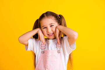 Photo of charming pretty school girl wear summer overall smiling arms cheeks isolated yellow color...