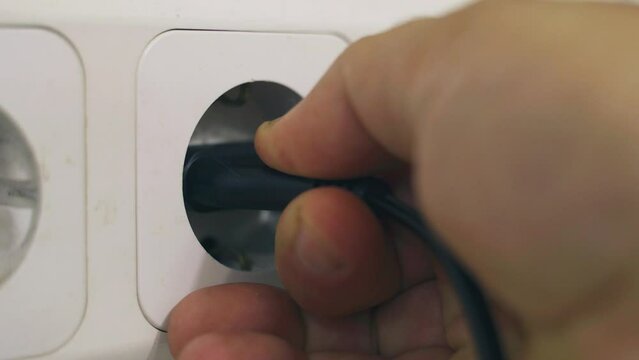 The hand turns off the device from the electrical network. Close-up of a hand removing a plug from an outlet.