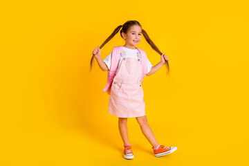 Photo of cute sweet school girl wear summer overall backpack walking hands tails isolated yellow color background