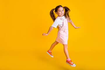 Fototapeta na wymiar Photo of pretty cute school girl wear summer overall jumping high empty space isolated yellow color background