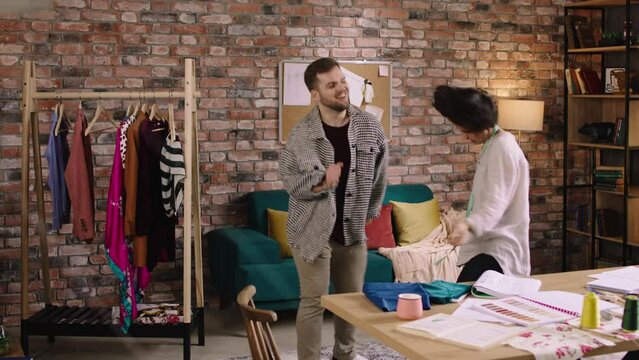 Two people in a tailors office are dancing and bopping their heads as they are enjoying eachothers company and looking very happy