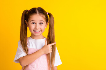 Photo of pretty cute school girl wear summer outfit pointing empty space isolated yellow color...