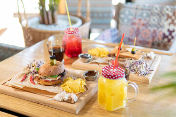 Beef patty burger, bacon, cheese, tomato, greens, pickle, goose pate sandwich, red cabbage salad, hot pepper, fries, corn chips, ketchup, orange and cherry juice