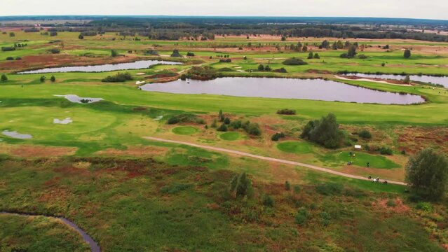 Aerial view of a flat green surface with a golf course and big ponds. A giant green forest in the background. High quality 4k footage