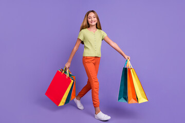 Full size profile photo of positive adorable girl hold packages walk isolated on violet color background