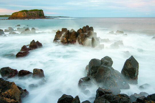 Long exposure of waves over sharp rocks with an island in the background