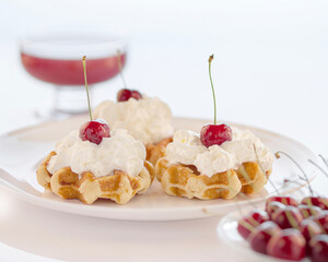 Light summer dessert with Dutch waffles with white cream, ripe cherries, on a white background