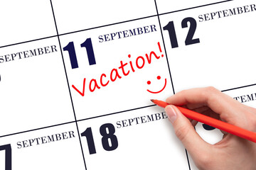 A hand writing a VACATION text and drawing a smiling face on a calendar date 11 September . Vacation planning concept.