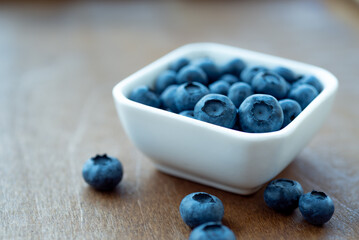 Fresh blueberries in a white bowl on wooden surface background. Concept for healthy nutrition.
