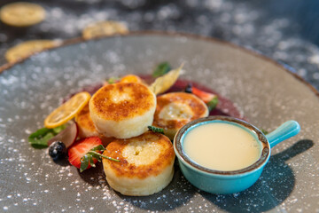 Cheesecakes with condensed milk and strawberries on a gray plate standing on a dark table