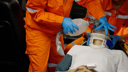 Asian emergency medical technician (EMT) or paramedic giving emergency oxygen with patient in ambulance car