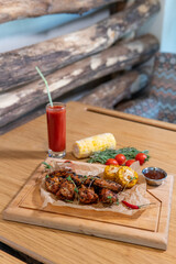 Chicken wings with barbecue sauce, hot pepper, microgreens, corn, tomato juice on a wooden board