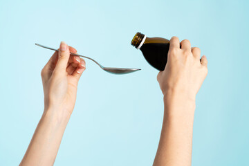 Image of hands with table spoon and bottle of medication.