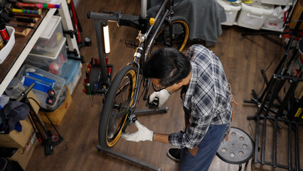 Top view of Asian senior man owner repairing and checking wheels and gears of bicycle while...
