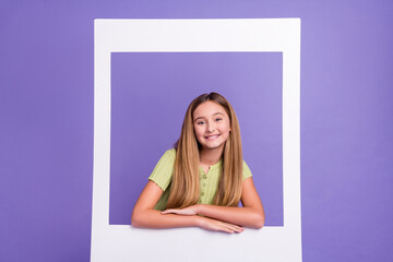 Portrait of adorable friendly pupil toothy smile look through paper album card isolated on purple...