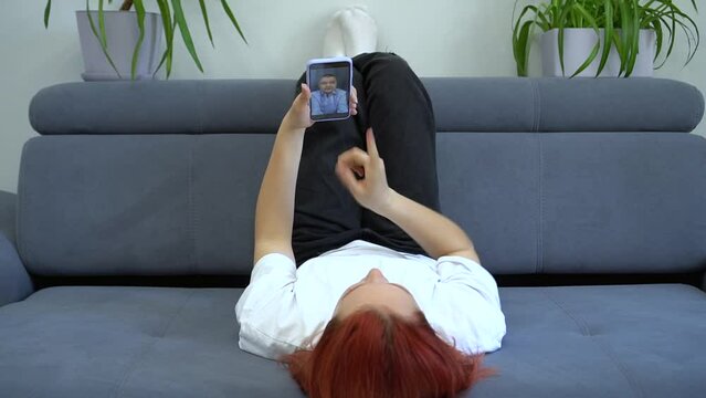 A teenage girl lies at home on the couch and communicates via video chat on the phone with her boyfriend. The concept of first love and virtual communication of teenagers.