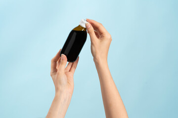 Image of hands holding a brown bottle of liquid cold medication. Bottle without label for product...