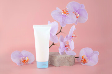 Obraz na płótnie Canvas skin care product. White cream tube on travertine stone next to an orchid flower on light pink background, layout. Cosmetic cream or lotion is handmade skin care product. Exotic natural cosmetics.
