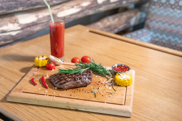 Grilled ribeye with rosemary, ajika, hot pepper, corn, tomato juice on a wooden board