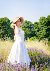 portrait of a beautiful sexy smiling woman &nbsp;in straw hat and white dress walking in lavender field