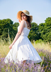 portrait of a beautiful sexy smiling woman  in straw hat and white dress walking in lavender field