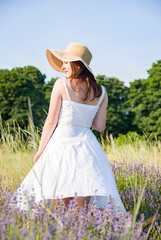 portrait of a beautiful sexy smiling woman  in straw hat and white dress walking in lavender field