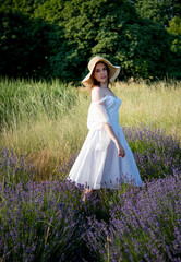 Obraz na płótnie Canvas portrait of a beautiful sexy smiling woman  in straw hat and white dress walking in lavender field