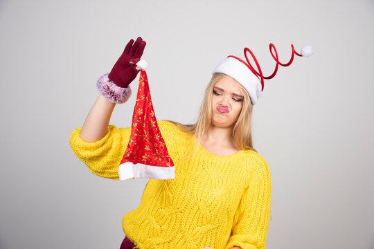 Blonde woman in yellow sweater looking at Santa hat disgustingly