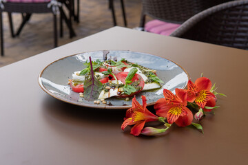 Mozzarella with tomatoes under pesto sauce, on a dark table, flowers lie nearby