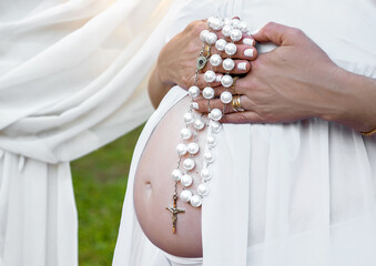 close up on pregnant woman's belly holding rosary of Christ.