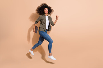 Fototapeta na wymiar Full length body size view of attractive cheerful girl jumping carrying laptop running isolated over beige pastel color background
