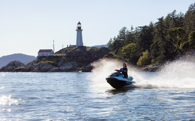 Fototapeta premium Adventurous Caucasian Woman on water scooter riding in the Ocean. Lighthouse park in background. West Vancouver, British Columbia, Canada.