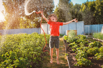 boy child jumping splashing hose water in the backyard in the garden in summer at sunset in the sunshine having fun summer