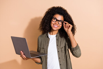Photo of young african woman curious look empty space hold laptop think plan isolated over beige...