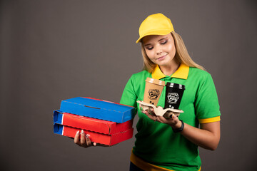 Deliverywoman looking on cups of coffee and holding cardboards of pizza