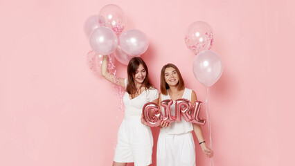 Portrait of happy two young women, dressed in a white, holdings a balloons, over pink background. Space for text.