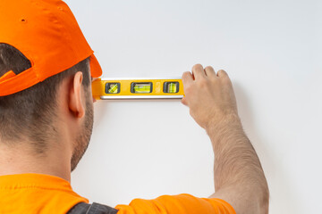 Worker using a ruler with a water level. Staff in a uniform cap, orange t-shirt, and overalls on a...