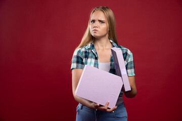 Blonde girl holds tight a gift box and looks confused and dissatisfied