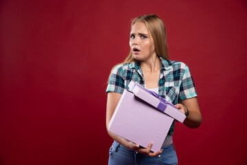 Blonde girl holds tight a gift box and looks confused and dissatisfied