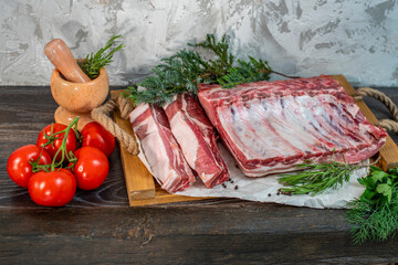 Raw pork loin, bacon with ribs on a wooden board, spice mortar, and pestle, rosemary, tomatoes. Pieces of meat, ingredients for cooking. Protein nutrition, a diet with fresh herbs and vegetables
