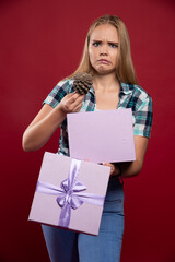 Blonde girl takes out an oak tree cone from the gift box and looks dissatisfied