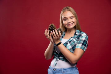 Blonde girl holds oak tree cone in the hand and looks positive and joyful