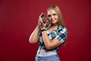 Blonde girl holds oak tree cone in the hand and looks positive and joyful