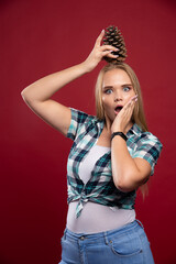 Blonde girl holds oak tree cone at her head and gives surprized poses