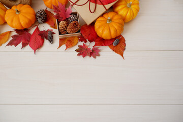 Autumn seasonal concept background. Autumn leaves, pumpkin and gift box on white wooden background. Thanks giving, Halloween and Autumn event decorative elements. 