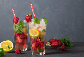 Cold bright strawberry Mojito cocktail with mint, lemon slices, ice cubes and drinking straw on gray background