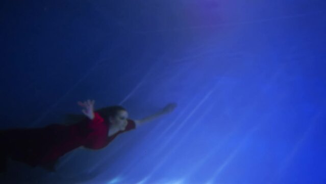 Beautiful free diver woman swimming in long red evening dress under water alone 
