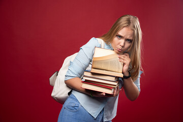 Blonde schoolgirl holding a heavy pile of books and looks tired