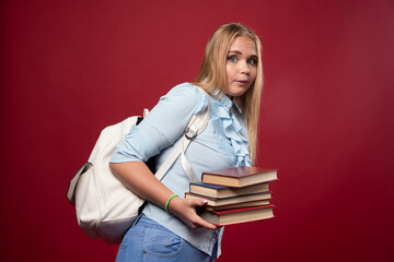 Blonde schoolgirl holding a heavy pile of books and looks tired