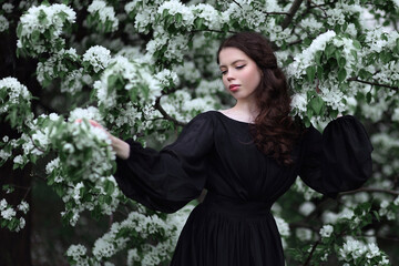 Young woman with long curly hair in black dress among blooming trees